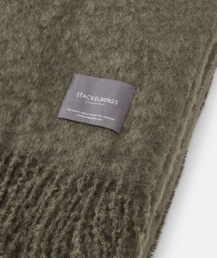 Close-up of the Stackelbergs logo on a luxurious green marble Mohair plaid on a white backdrop.