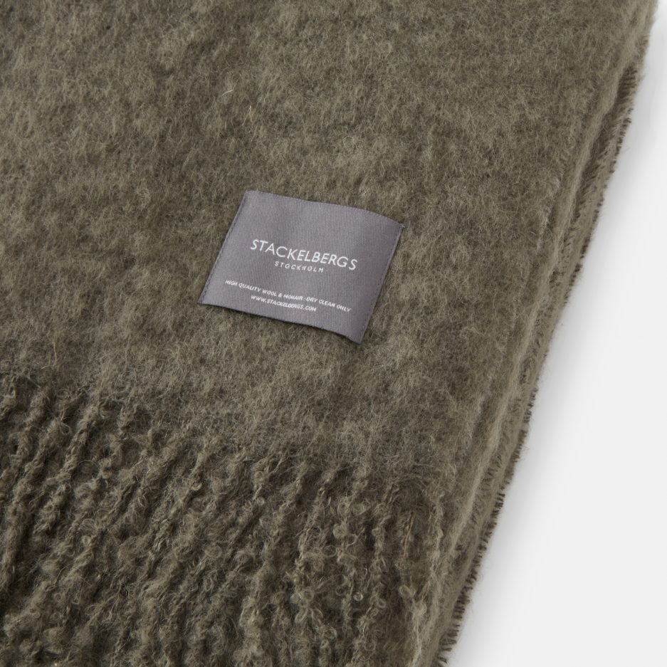 Close-up of the Stackelbergs logo on a luxurious green marble Mohair plaid on a white backdrop.