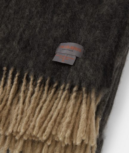 Close-up of the Stackelbergs logo on a luxurious sand & black melange Mohair plaid on a white backdrop.