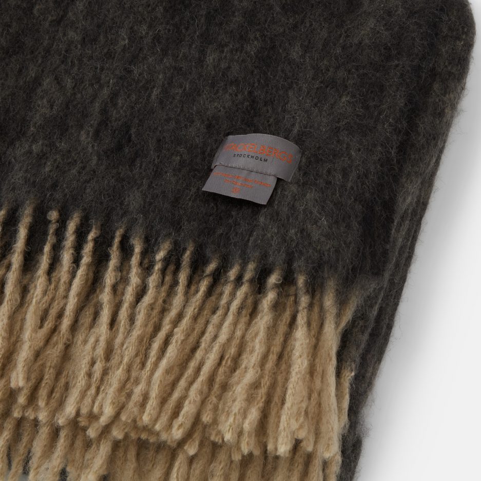 Close-up of the Stackelbergs logo on a luxurious sand & black melange Mohair plaid on a white backdrop.