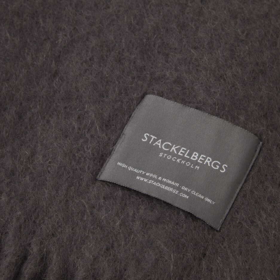 Close-up of the Stackelbergs logo on a luxurious charcoal Mohair plaid on a white backdrop.