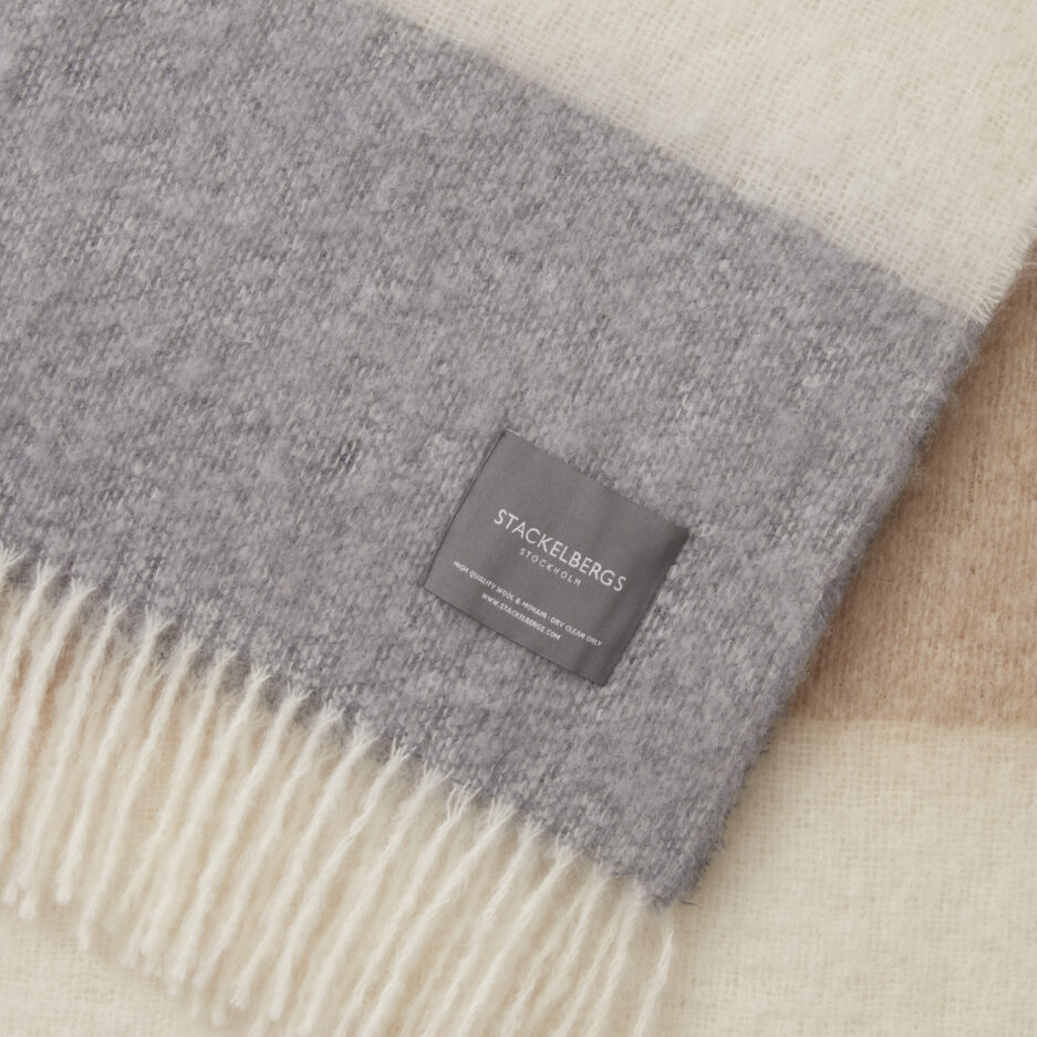 Close-up of the Stackelbergs logo on a luxurious camel & skiffer striped Mohair plaid on a white backdrop.