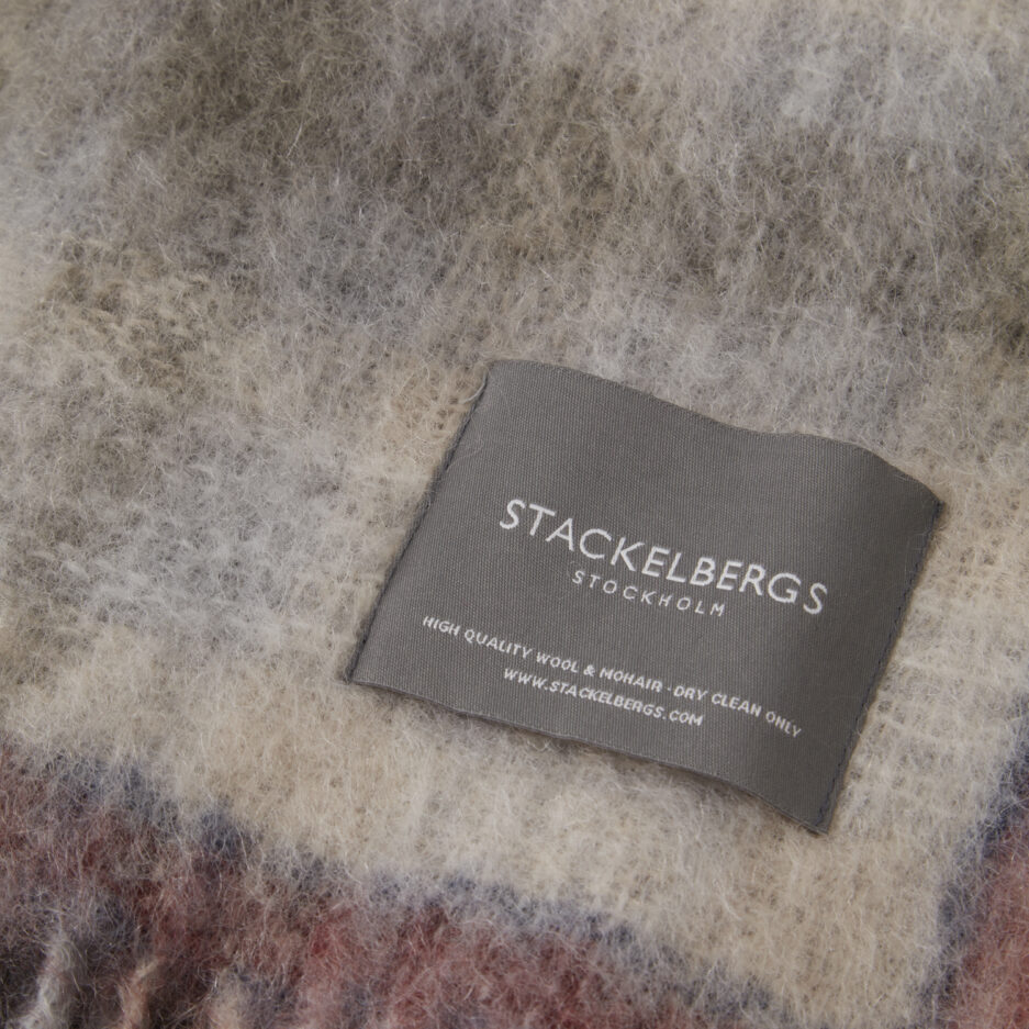 Close-up of the Stackelbergs logo on a luxurious camelbeige & fried check Mohair plaid on a white backdrop.