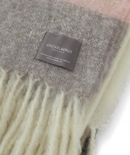 Close-up of the Stackelbergs logo on a luxurious stripe brown, black and rose Mohair plaid on a white backdrop.