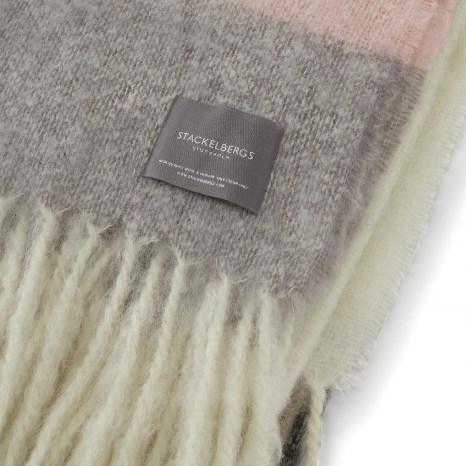 Close-up of the Stackelbergs logo on a luxurious stripe brown, black and rose Mohair plaid on a white backdrop.