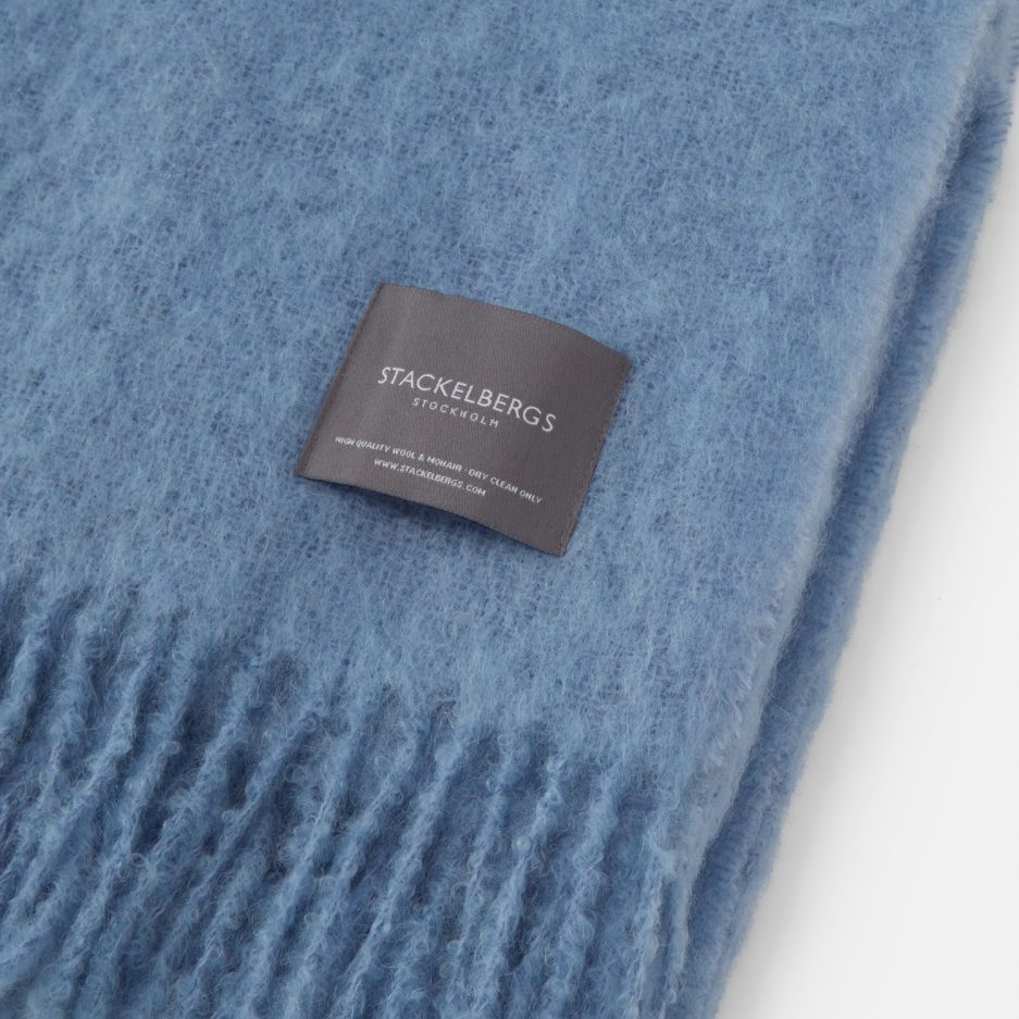 Close-up of the Stackelbergs logo on a luxurious sky blue Mohair plaid on a white backdrop.