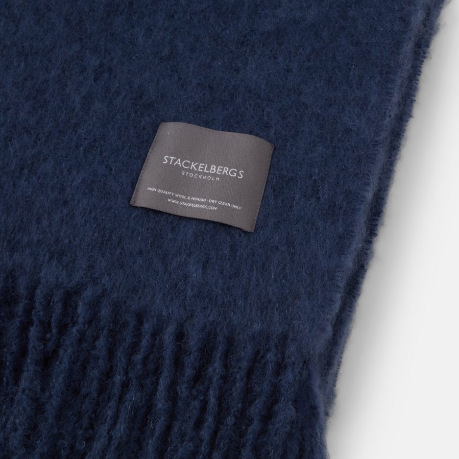 Close-up of the Stackelbergs logo on a luxurious denim dark blue Mohair plaid on a white backdrop.