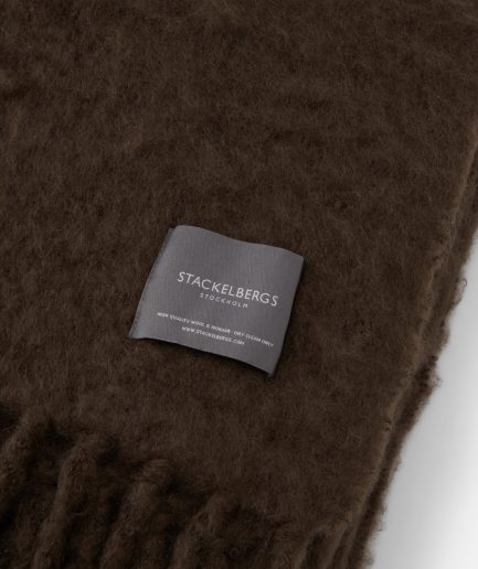 Close-up of the Stackelbergs logo on a luxurious brown chocolate Mohair plaid on a white backdrop.