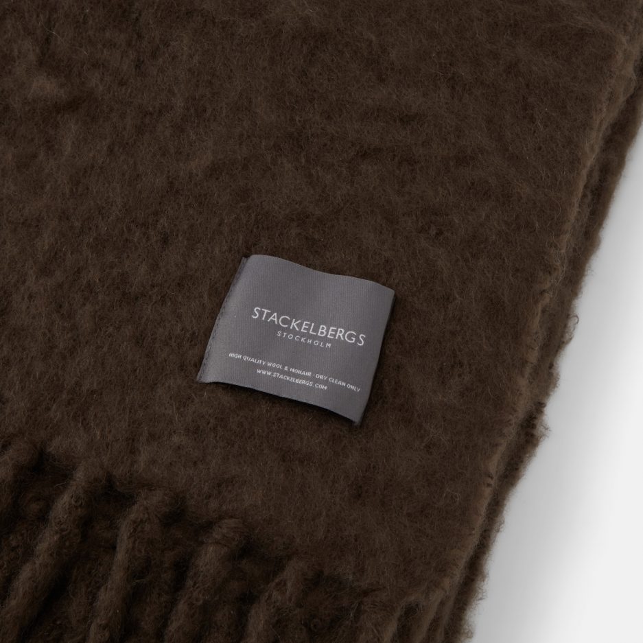 Close-up of the Stackelbergs logo on a luxurious brown chocolate Mohair plaid on a white backdrop.