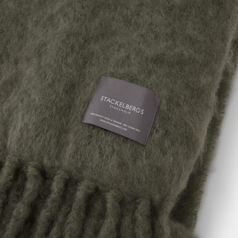 Close-up of the Stackelbergs logo on a luxurious green marble Mohair plaid on a white backdrop.