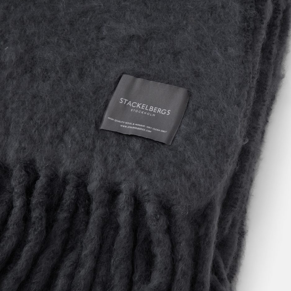 Close-up of the Stackelbergs logo on a luxurious grey storm Mohair plaid on a white backdrop.