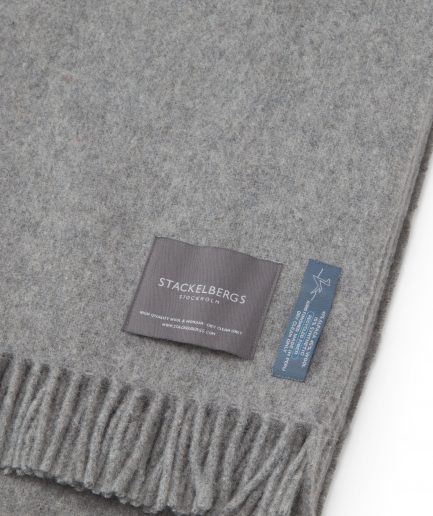 Close-up of the Stackelbergs logo on a luxurious alpaca light grey recycled Mohair plaid on a white backdrop.