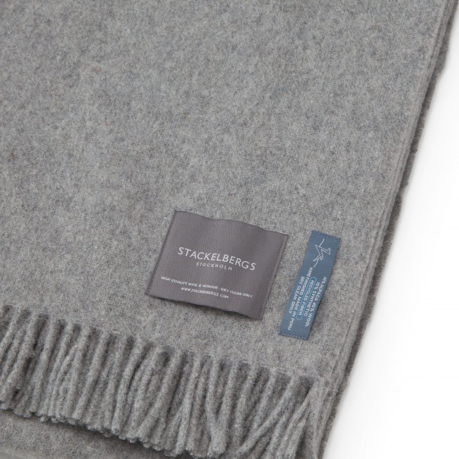 Close-up of the Stackelbergs logo on a luxurious alpaca light grey recycled Mohair plaid on a white backdrop.