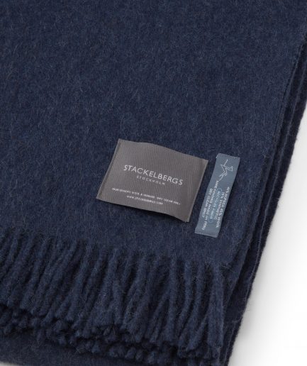 Close-up of the Stackelbergs logo on a luxurious alpaca azur recycled Mohair plaid on a white backdrop.