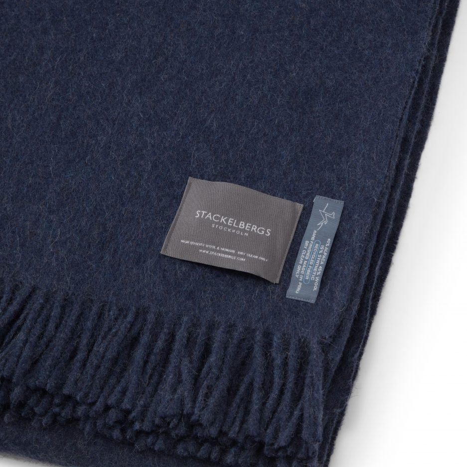 Close-up of the Stackelbergs logo on a luxurious alpaca azur recycled Mohair plaid on a white backdrop.