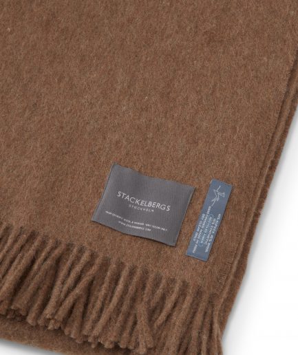 Close-up of the Stackelbergs logo on a luxurious alpaca brown recycled Mohair plaid on a white backdrop.