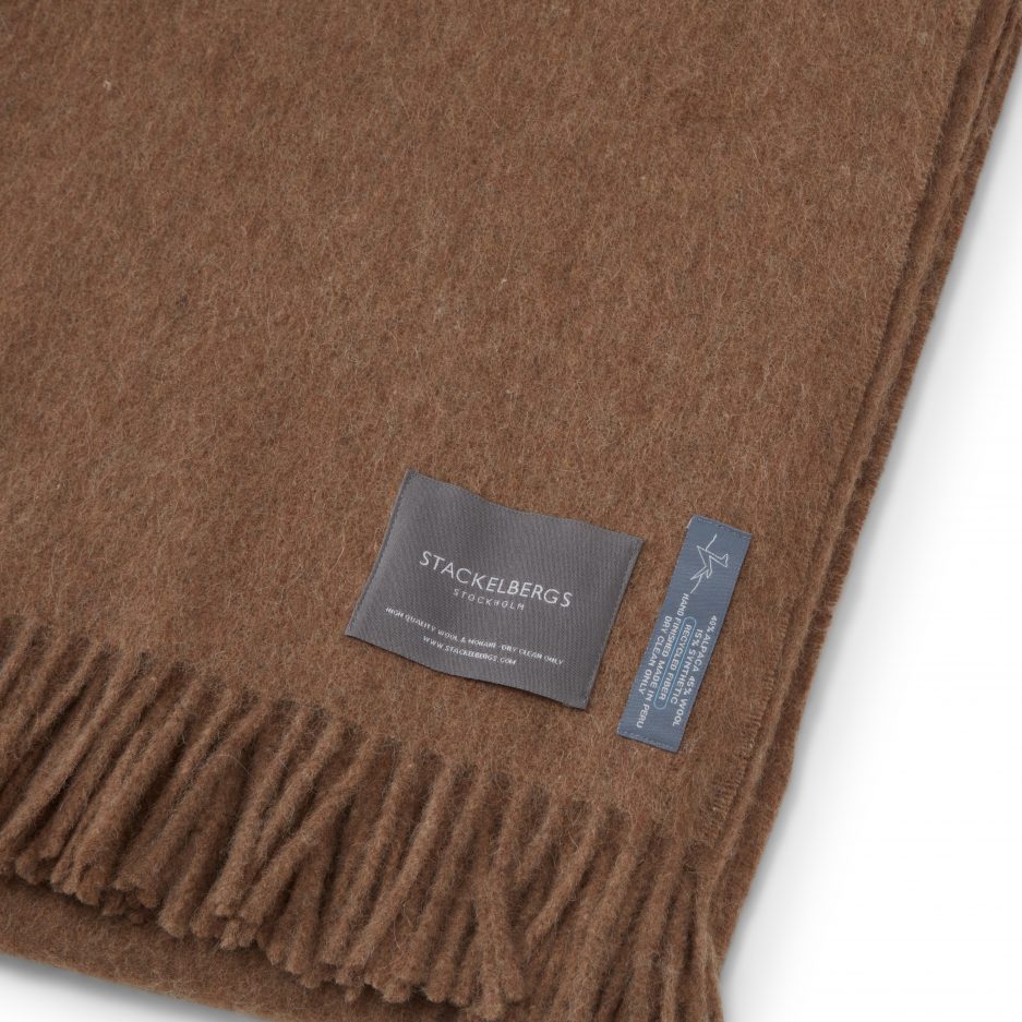 Close-up of the Stackelbergs logo on a luxurious alpaca brown recycled Mohair plaid on a white backdrop.