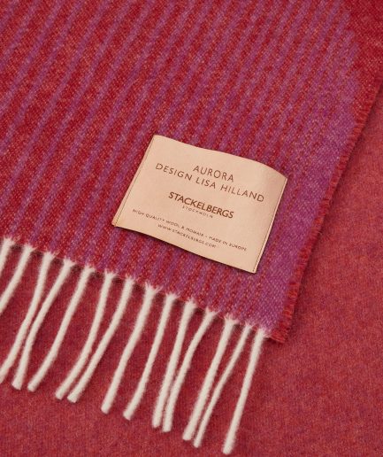 Close-up of the Stackelbergs logo on a luxurious Camino Red, Violet & Orange wool plaid Designed by Lisa Hilland on a white backdrop.