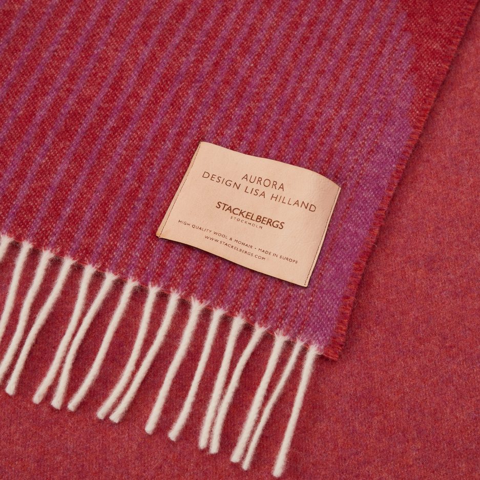 Close-up of the Stackelbergs logo on a luxurious Camino Red, Violet & Orange wool plaid Designed by Lisa Hilland on a white backdrop.