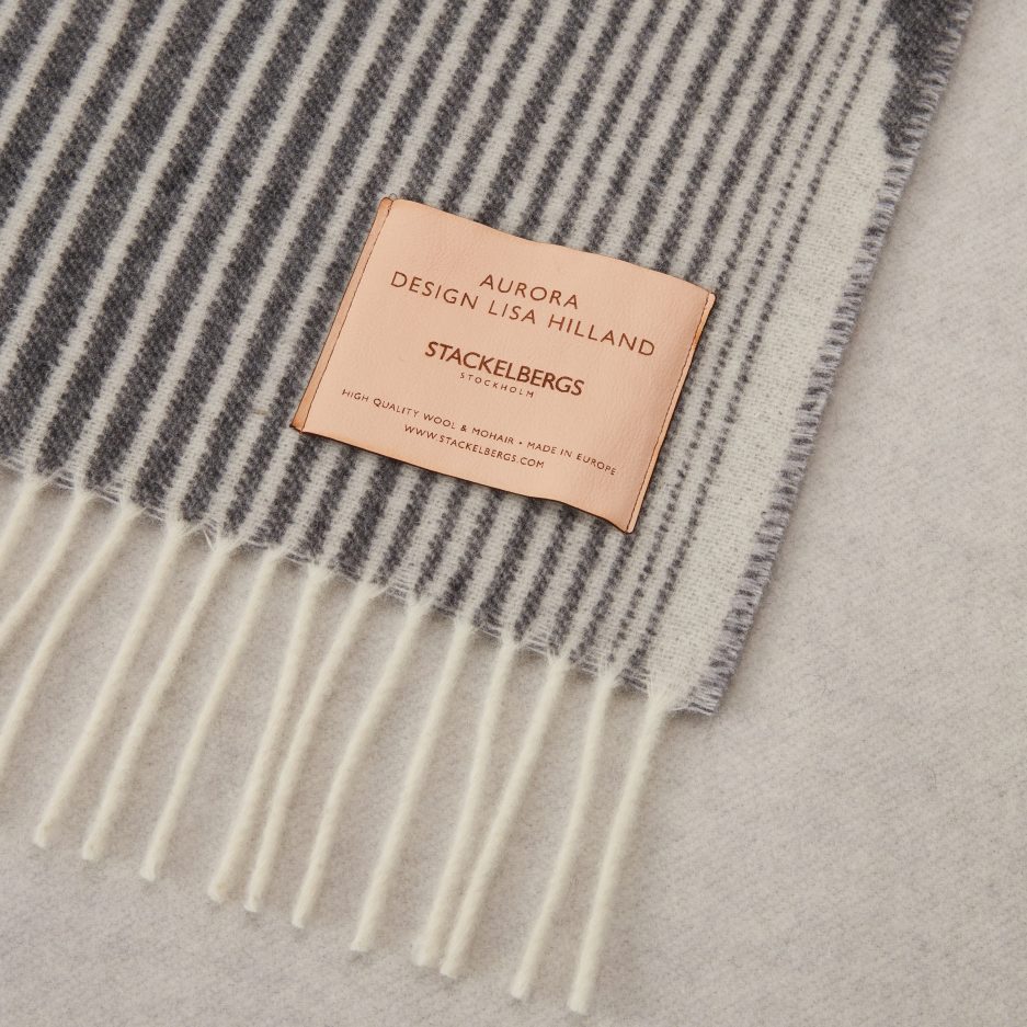 Close-up of the Stackelbergs logo on a luxurious Midnight, Charcoal & Cool Grey wool plaid Designed by Lisa Hilland on a white backdrop.