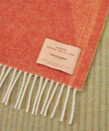 Close-up of the Stackelbergs logo on a luxurious Orange, Grass Green & Sky Blue wool plaid Designed by Lisa Hilland on a white backdrop.