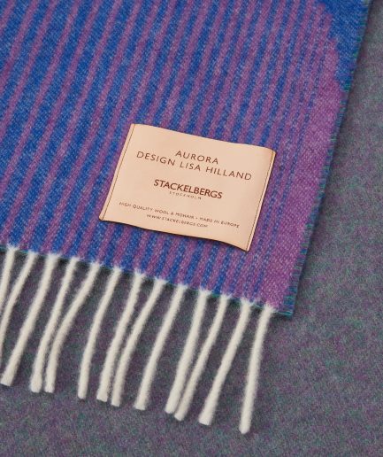 Close-up of the Stackelbergs logo on a luxurious Dark Indigo, Violet & Rose wool plaid Designed by Lisa Hilland on a white backdrop.