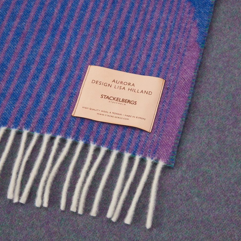 Close-up of the Stackelbergs logo on a luxurious Dark Indigo, Violet & Rose wool plaid Designed by Lisa Hilland on a white backdrop.