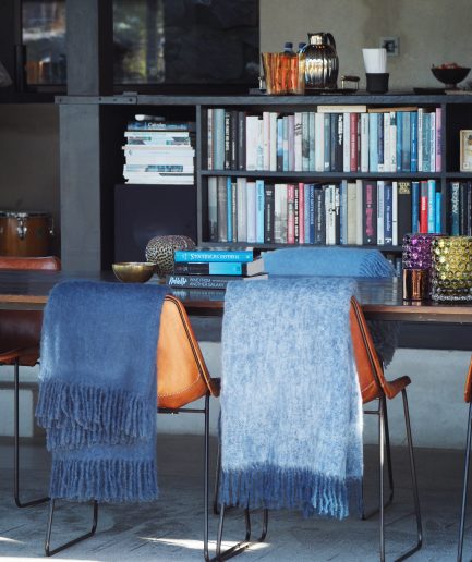 A sun filled room with a bookshelf and two luxurious Mohair plaids in deep blue and light blue hanging of two chairs.