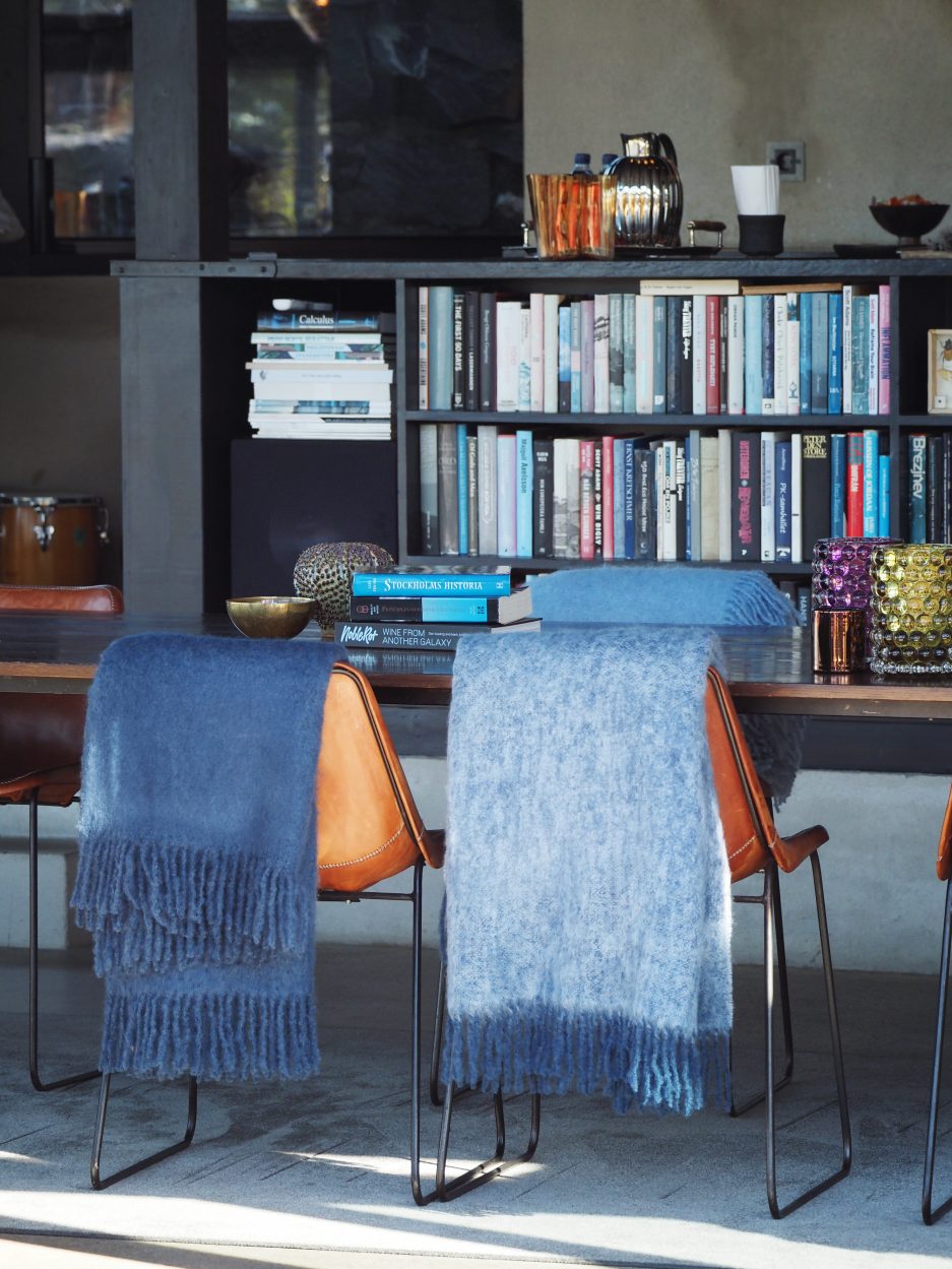 A sun filled room with a bookshelf and two luxurious Mohair plaids in deep blue and light blue hanging of two chairs.